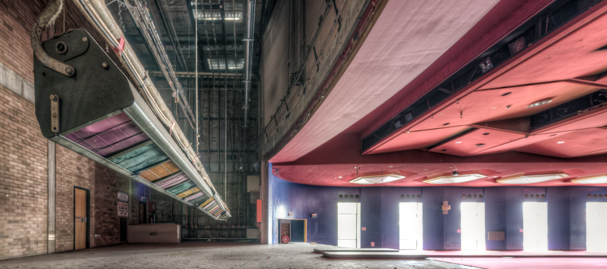 Interior of the abandoned Bankstown RSL auditorium, showcasing its vibrant red ceiling, colorful stage rigging, and empty performance space before demolition. Captured by Lost Collective.