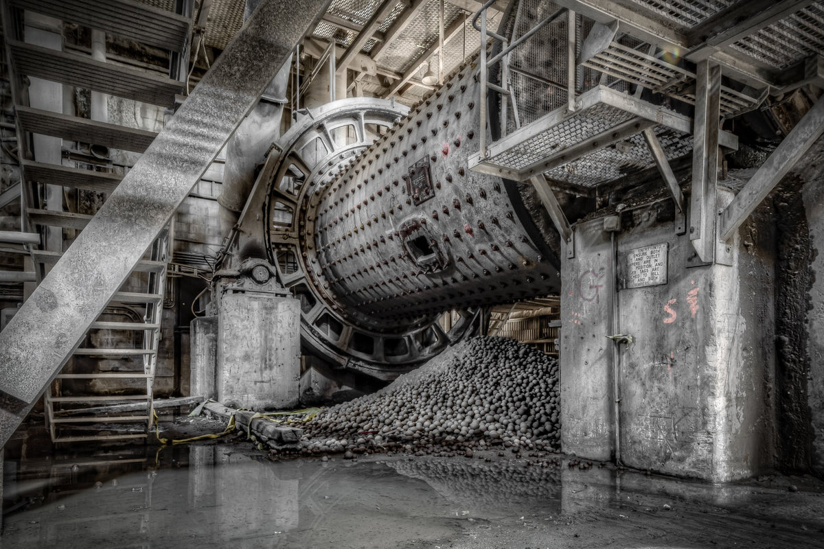 A cylindrical ball mill at Kandos Cement Works, its load of steel grinding balls spilled across the floor, steel stairs behind.