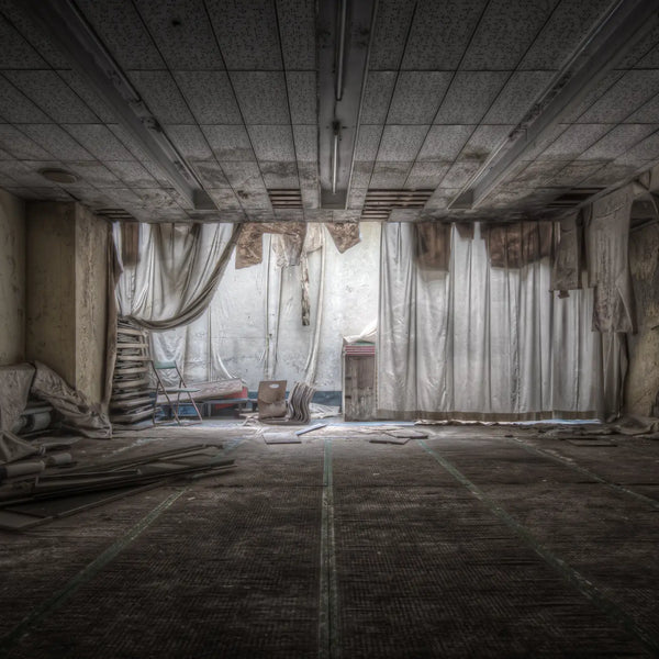 An empty function room inside Kinugawa Kan, cream fabric drapes fallen from the ceiling, a step ladder against the back wall, debris scattered across the grid-tiled floor.