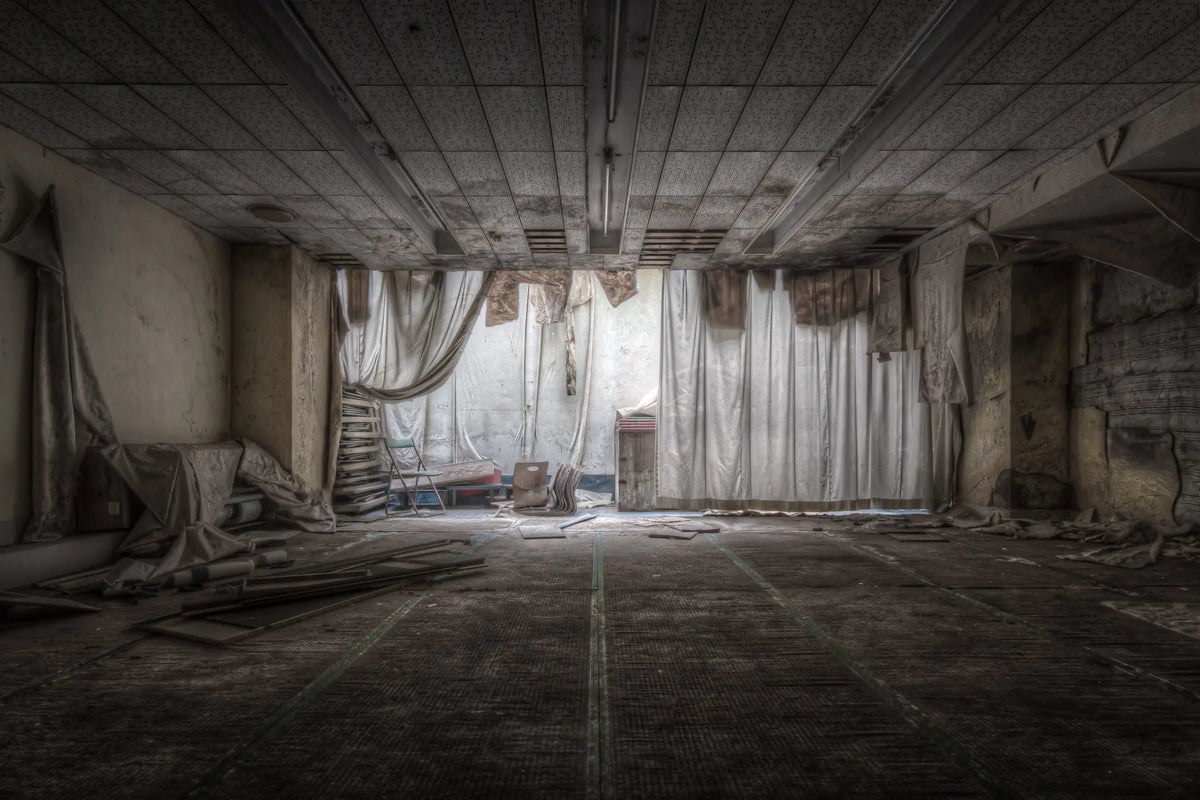 An empty function room inside Kinugawa Kan, cream fabric drapes fallen from the ceiling, a step ladder against the back wall, debris scattered across the grid-tiled floor.