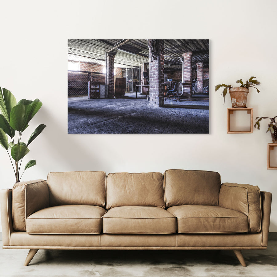 A coiled rope hangs from a brick column in the basement of the administration building at Awaba Colliery, with an overturned office chair on a desk and shadows across the concrete floor.