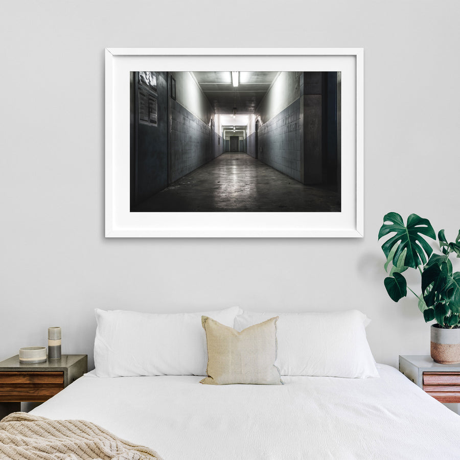 A narrow corridor at Awaba Colliery with fluorescent lights still burning along the ceiling, light-grey tiled walls, a concrete floor, and a closed door at the far end.
