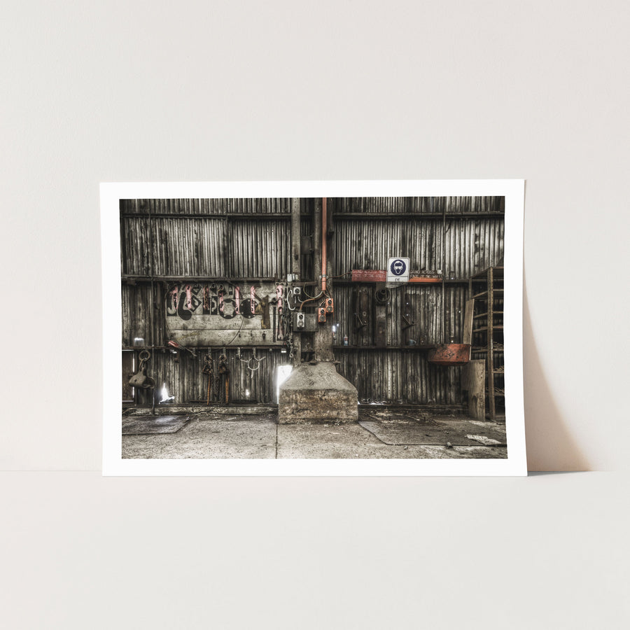 Workshop wall at Awaba Colliery showing a pegboard with remaining lifting gear, an empty grinder base, red safety signs, and graffiti on wooden planking.