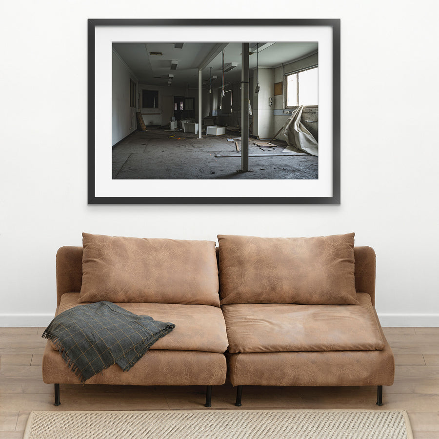Stripped interior room at the former Bradmill factory in Yarraville, with a white support column, scattered cabinetry panels and cables on a bare concrete floor, and daylight entering from a window on the right.