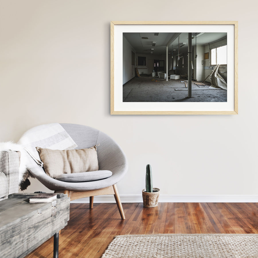 Stripped interior room at the former Bradmill factory in Yarraville, with a white support column, scattered cabinetry panels and cables on a bare concrete floor, and daylight entering from a window on the right.