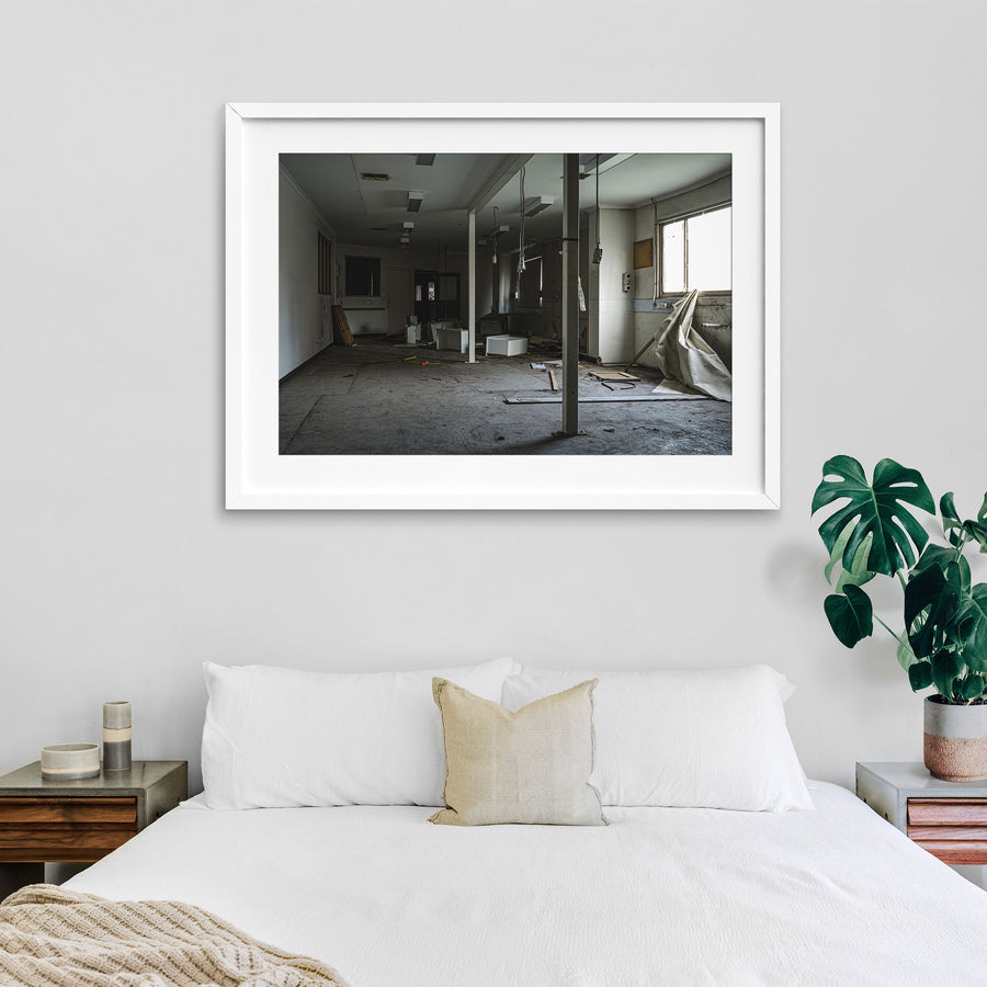 Stripped interior room at the former Bradmill factory in Yarraville, with a white support column, scattered cabinetry panels and cables on a bare concrete floor, and daylight entering from a window on the right.
