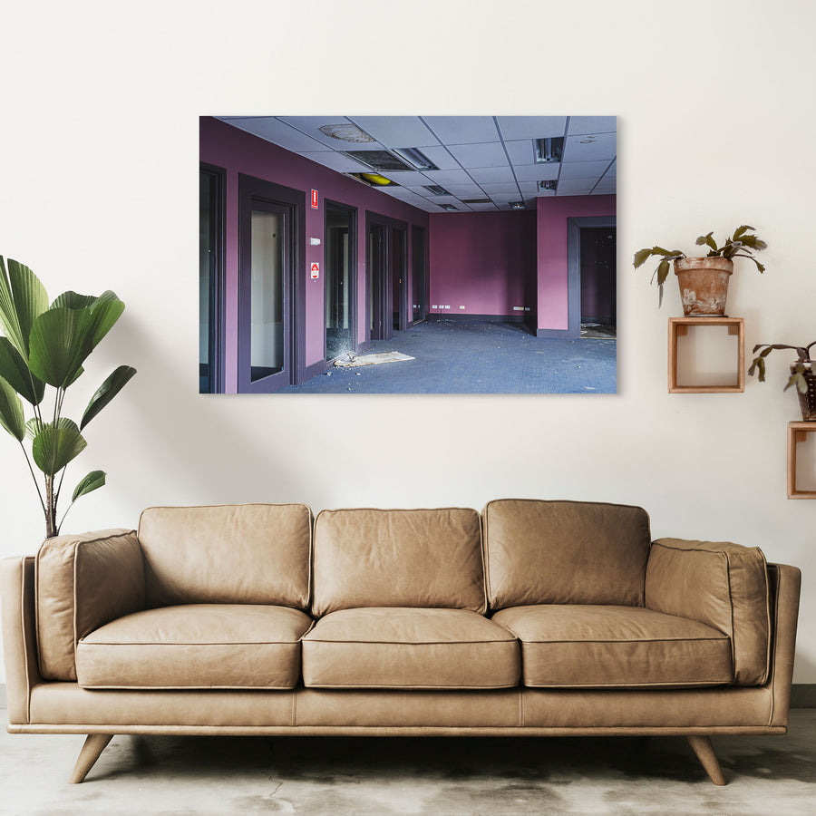 Empty office corridor at the former Bradmill factory in Yarraville, with mauve walls, grey carpet, glazed timber-framed doorways, a damaged suspended ceiling, and a red fire safety sign on the wall.