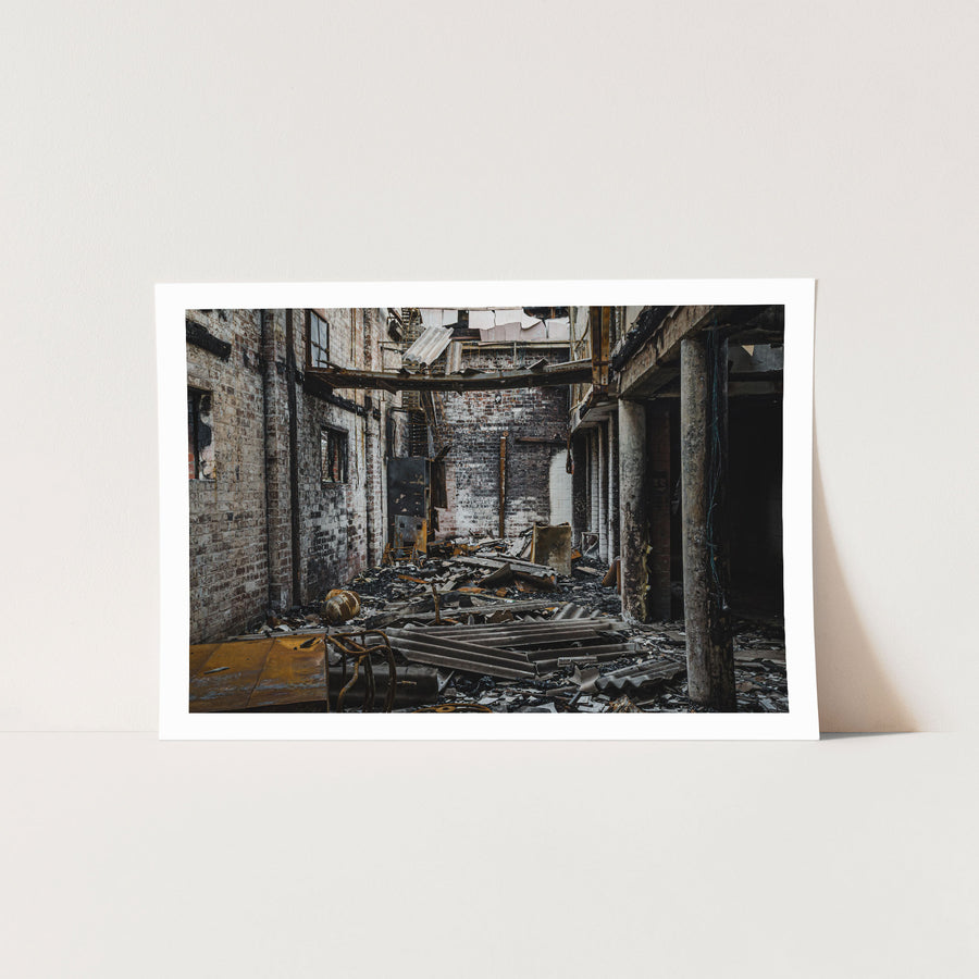 Gutted brick interior of a fire-damaged manufacturing building at the former Bradmill factory in Yarraville, with charred debris on the floor, soot-stained walls and exposed steel framing overhead.