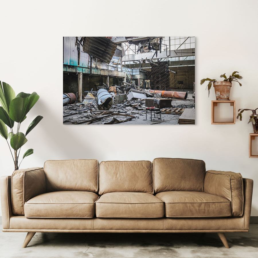 Fire-damaged manufacturing hall at the former Bradmill factory in Yarraville, with a collapsed roof, twisted metal sheeting, rusted cylindrical vessels, and a single chair on the debris-covered floor.