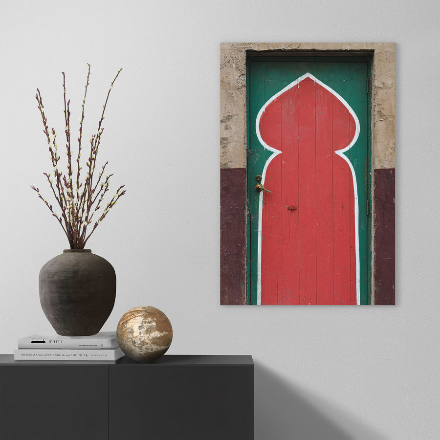 A painted timber door at the former Bradmill factory in Yarraville, with a tall red keyhole arch outlined in white on a green background, a worn brass lever handle on the left, and cracked render surrounding the frame.