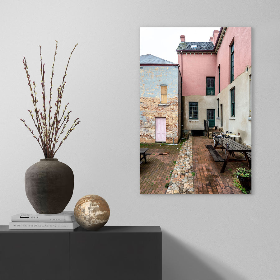 Brick courtyard with timber picnic tables, a pink-painted door and green sash windows at Braidwood Hotel, NSW.