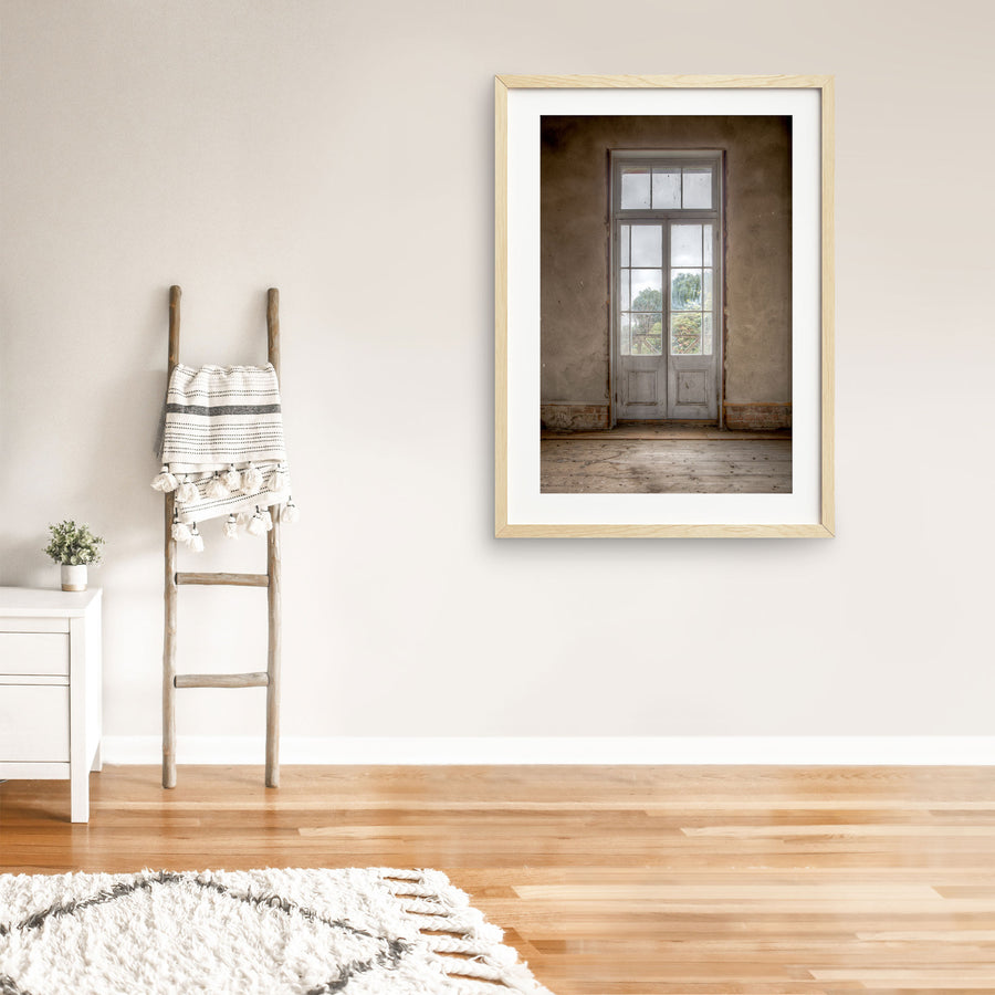 Dusty white-framed French doors with multiple glass panes and timber lower panels, set into a worn rendered wall at the Braidwood Hotel, with green trees visible beyond a timber railing.