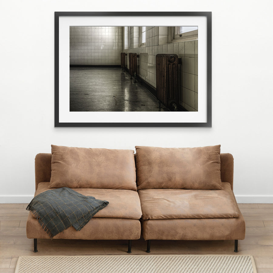Three cast-iron radiators along a tiled corridor wall at Callan Park, reflected in the polished concrete floor below.