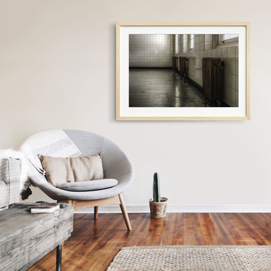 Three cast-iron radiators along a tiled corridor wall at Callan Park, reflected in the polished concrete floor below.