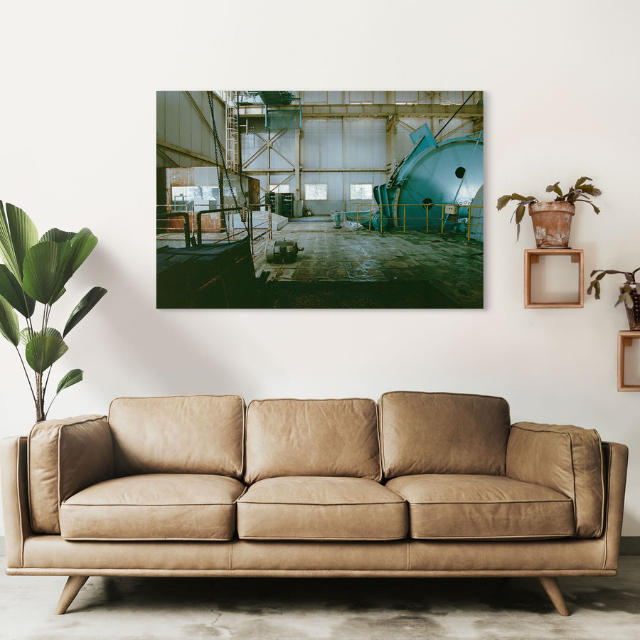 The sheave wheel, hoist drum and hanging chains of the winding house interior at Ikeshima Coal Mine, with a yellow-railed cylindrical vessel to the right and three rectangular windows along the far wall.