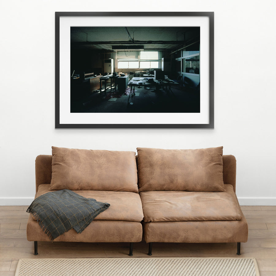 Interior of a derelict office at Ikeshima Coal Mine, with horizontal blinds casting banded light across paper-strewn desks, a large dark monitor, a white air conditioning unit, and a sagging ceiling with visible water damage.
