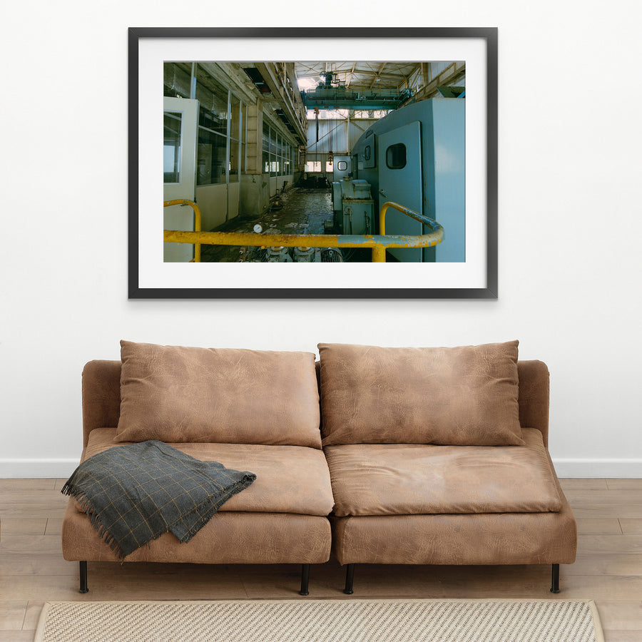 Interior of the winding house at Ikeshima Coal Mine, showing a light-blue winding engine with panelled doors, a teal overhead gantry crane, glass-paned windows, and a pressure gauge on the concrete floor.