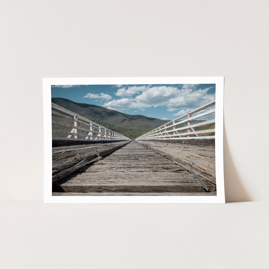Weathered timber deck planks and white handrails recede along McKillops Bridge toward the far wall of the Snowy River gorge at Deddick Valley.