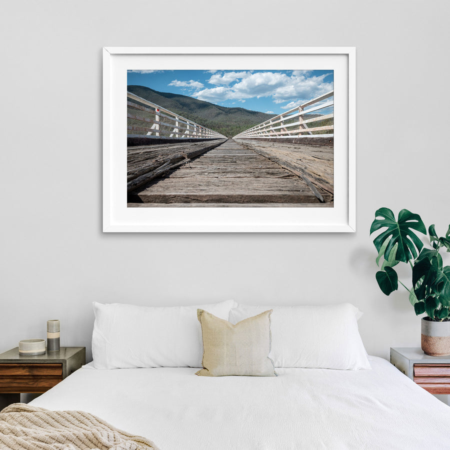 Weathered timber deck planks and white handrails recede along McKillops Bridge toward the far wall of the Snowy River gorge at Deddick Valley.