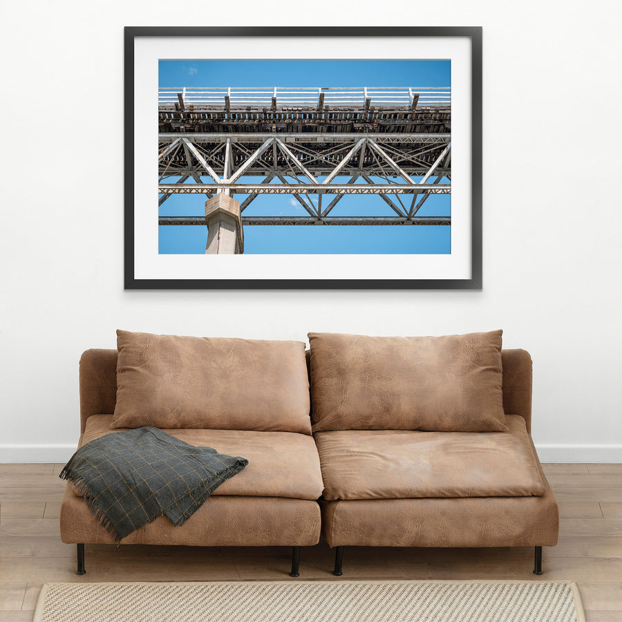 View from below McKillops Bridge in Deddick Valley, looking up at the electric-arc-welded steel Warren trusses and weathered timber decking against a clear sky, with a tall concrete pier at the left.