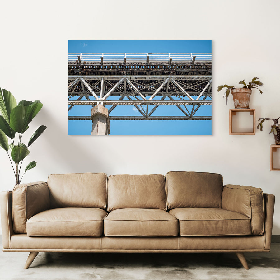 View from below McKillops Bridge in Deddick Valley, looking up at the electric-arc-welded steel Warren trusses and weathered timber decking against a clear sky, with a tall concrete pier at the left.