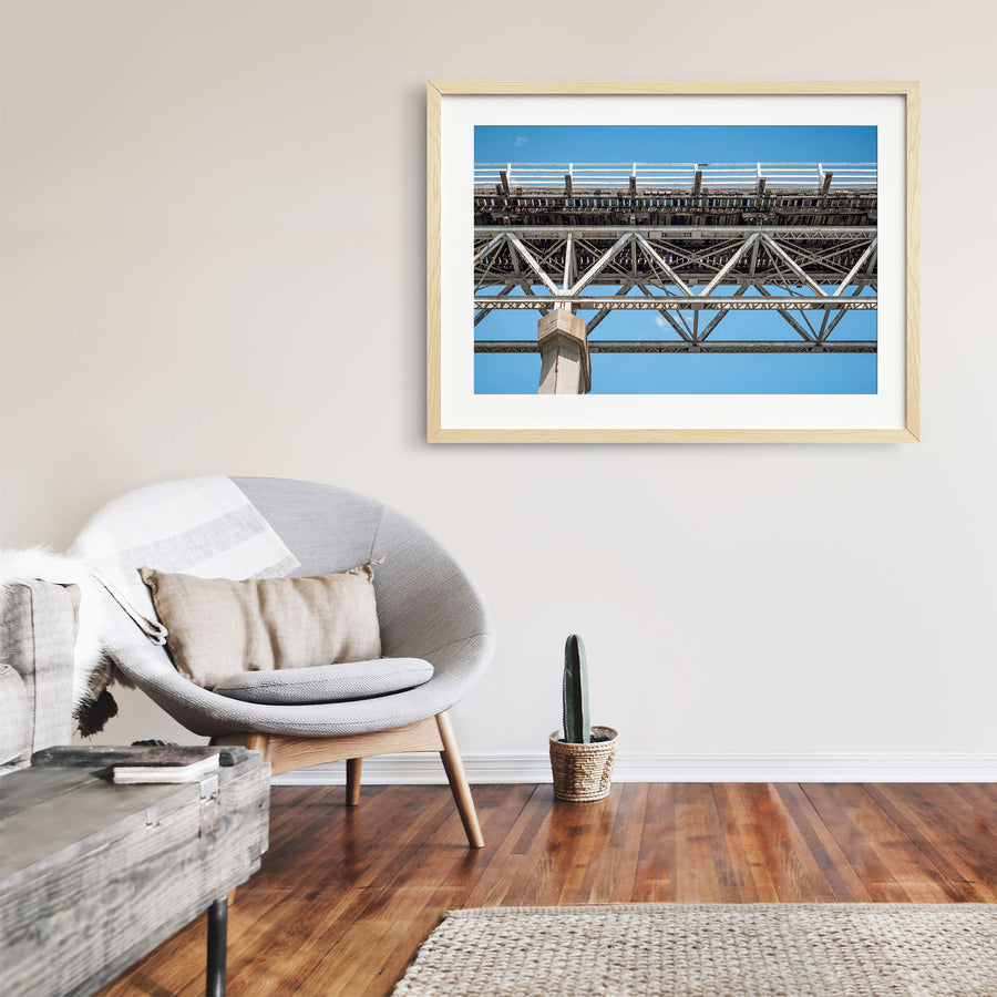 View from below McKillops Bridge in Deddick Valley, looking up at the electric-arc-welded steel Warren trusses and weathered timber decking against a clear sky, with a tall concrete pier at the left.