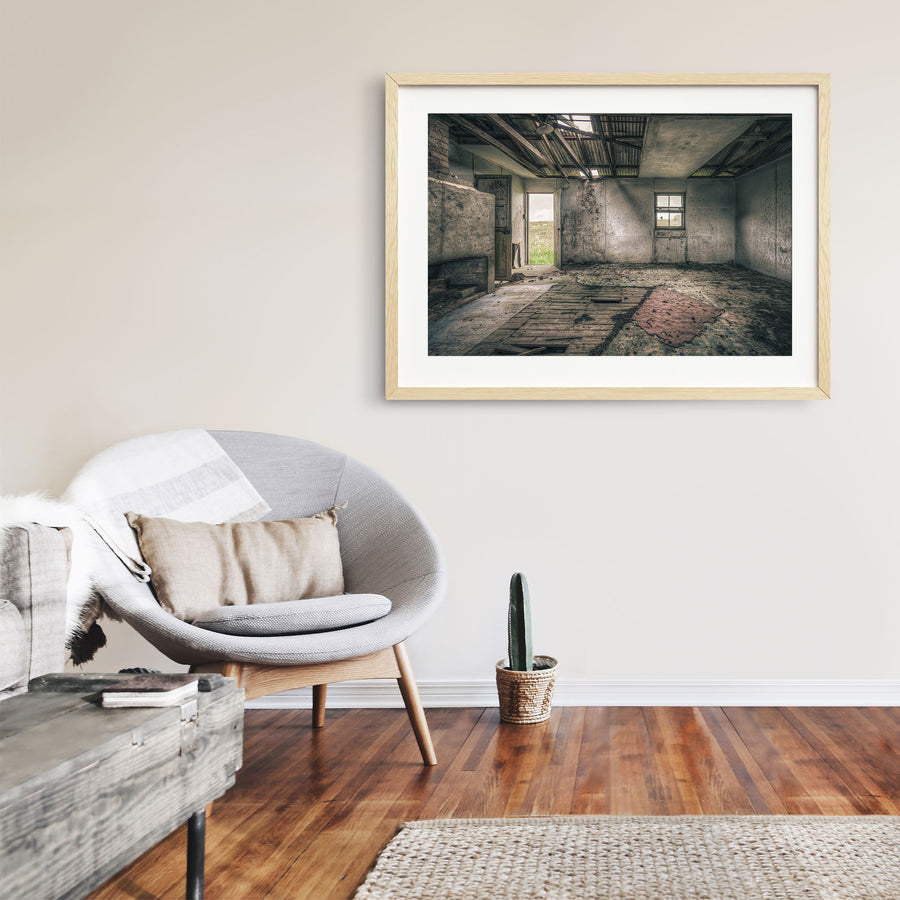 Interior of a derelict room at Jembaicumbene with a partly collapsed corrugated metal roof open to the sky, exposed timber rafters, rendered walls, a four-pane sash window, an open timber door to a paddock, and a torn red rug on broken floorboards.