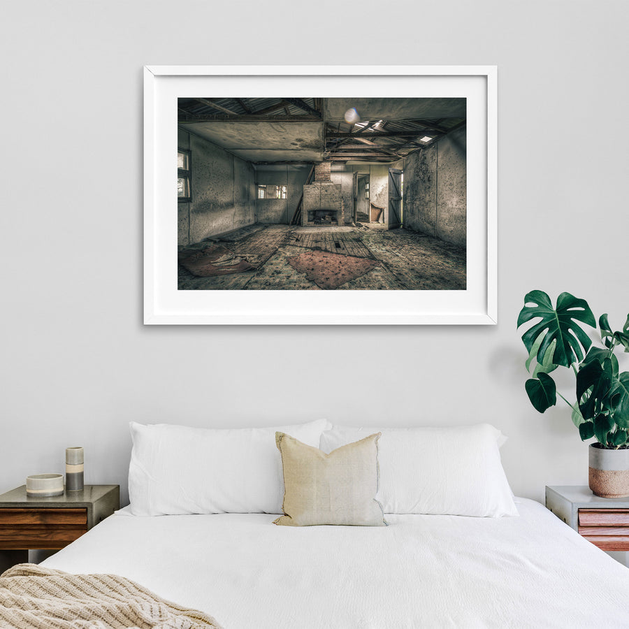 A rendered fireplace and brick chimney in a derelict room at Jembaicumbene, with whitewashed walls, a debris-strewn timber plank floor, and partly exposed roof framing overhead.
