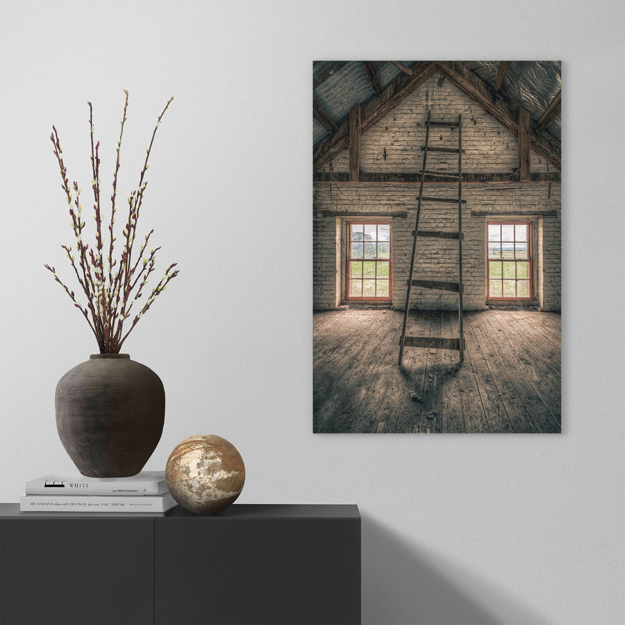 A timber ladder leans against a whitewashed brick gable wall rising to the roof apex inside the mill at Jembaicumbene, with two red-framed sash windows open to fields beyond.