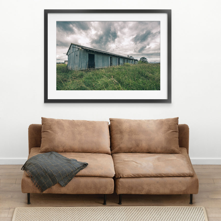 A weathered corrugated iron building with empty window openings and an open doorway stands in tall grass at Jembaicumbene, New South Wales.