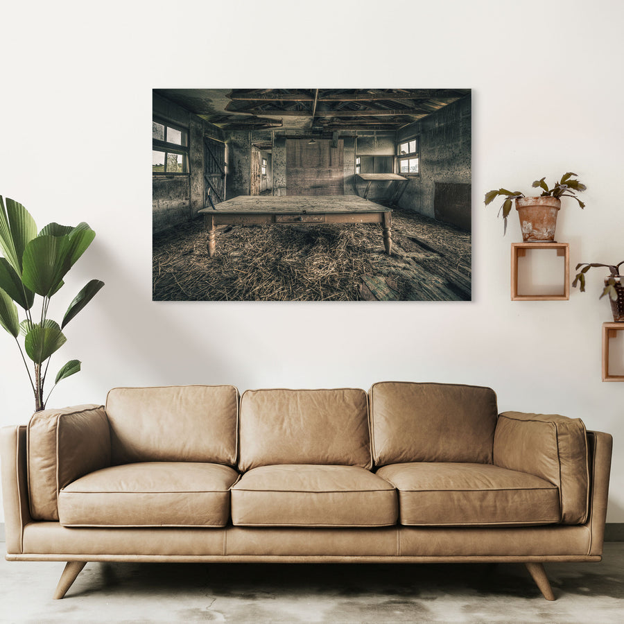 A long timber table with turned legs stands on a straw-strewn floor inside a derelict outbuilding at Mill Pond Farm, Jembaicumbene, with exposed rafters overhead and light entering from windows on either side.