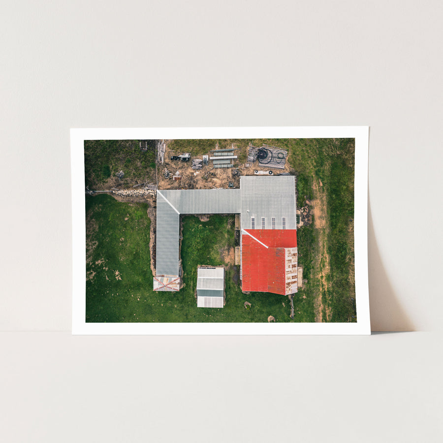 Aerial view of an L-shaped farm complex with grey and red corrugated iron roofing, surrounded by green paddocks at Jembaicumbene, New South Wales.