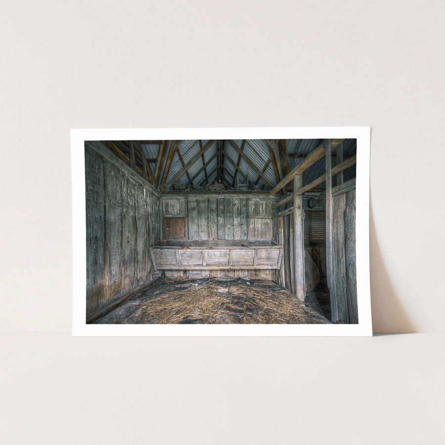 Feed trough and timber walls at Jembaicumbene barn, straw scattered across the dirt floor.
