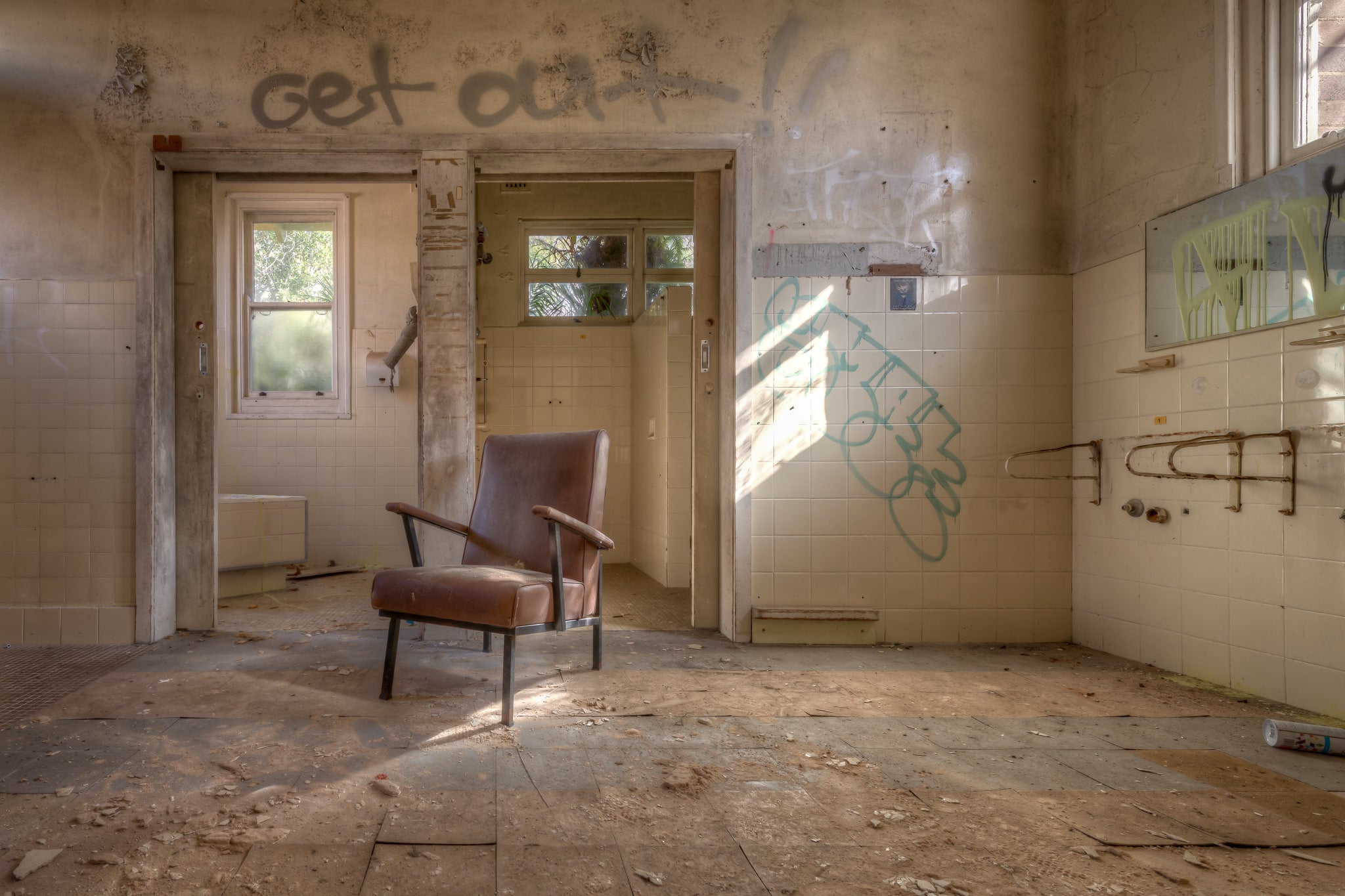 Bathrooms at Waterfall Sanatorium, a brown vinyl armchair sits centre-frame on a floor thick with plaster dust and debris.