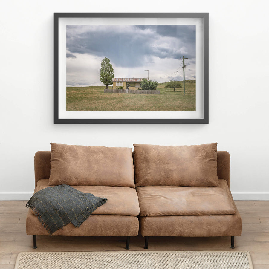 Home On the Range at A Place to Call Home, a long-vacant, lone farm cottage sits in a field beneath a distant rain cloud.