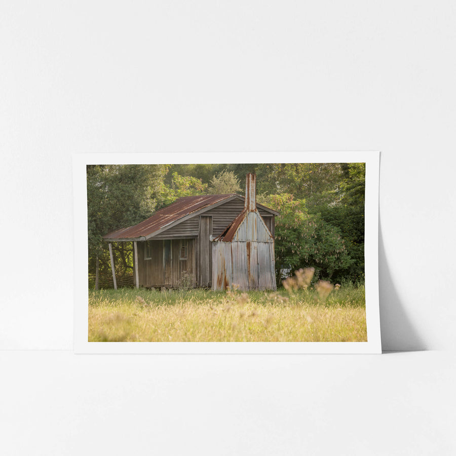 Hunter Hut at A Place to Call Home, a small timber and corrugated iron hut sits at the edge of a grass paddock in late.