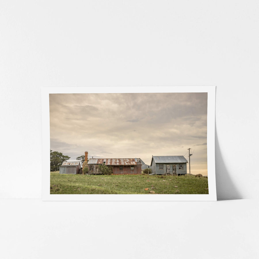 Numbla Vale Buildings at A Place to Call Home, a cluster of buildings sits on a green rise under heavy, layered cloud.