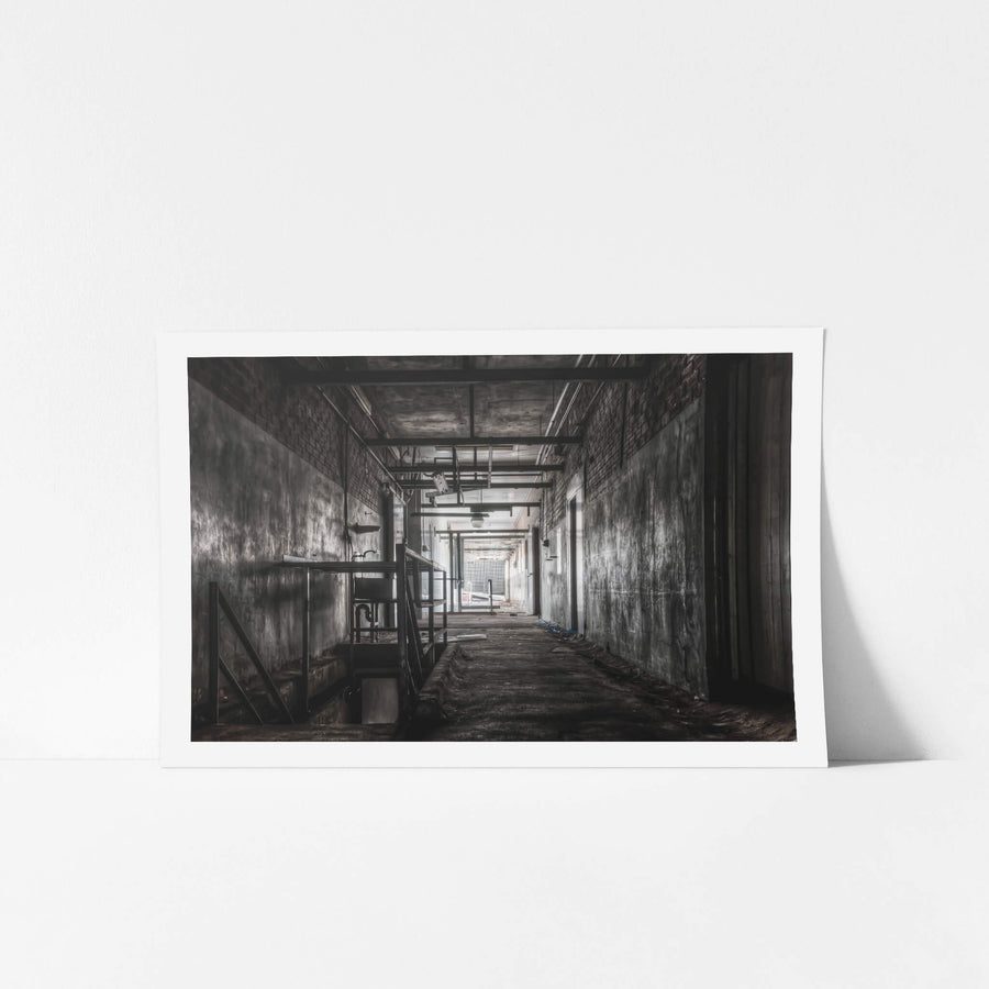 Downstairs Exit at Blayney Abattoir, a concrete corridor narrows toward a mesh gate at the far end, where grey light spills.
