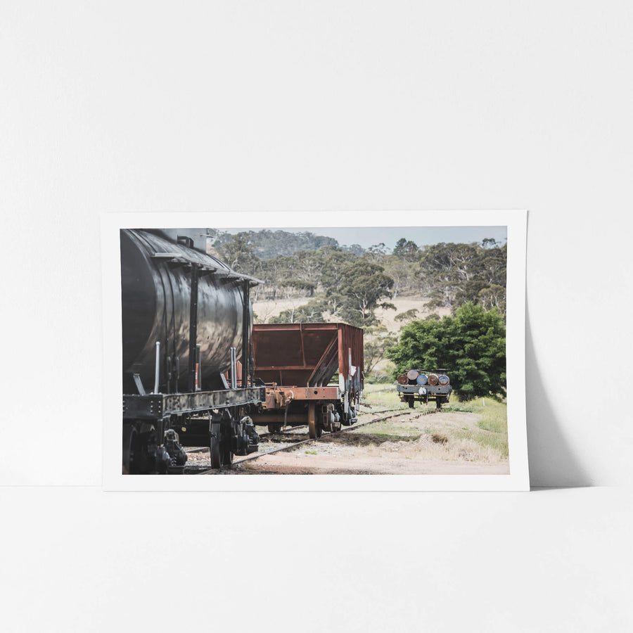 L Truck at Bombala Station, a black cylindrical tank wagon sits coupled to a rust-red hopper truck on a siding of worn rail.