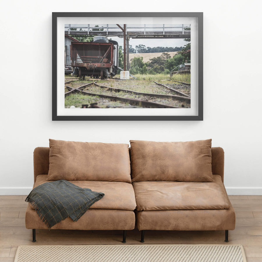 Upline at Bombala Station, a rusted hopper wagon sits low on the sidings beneath a steel and timber footbridge.