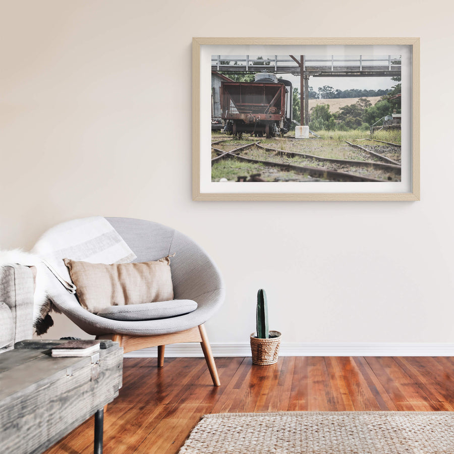 Upline at Bombala Station, a rusted hopper wagon sits low on the sidings beneath a steel and timber footbridge.