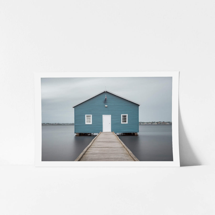 Crawley Edge Boatshed at Landscapes, a single blue timber boatshed sits on steel piles over flat grey water.