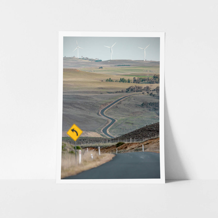 The Snowy River Way at Landscapes, a single lane of asphalt cuts through open grazing country, snaking down into a valley.
