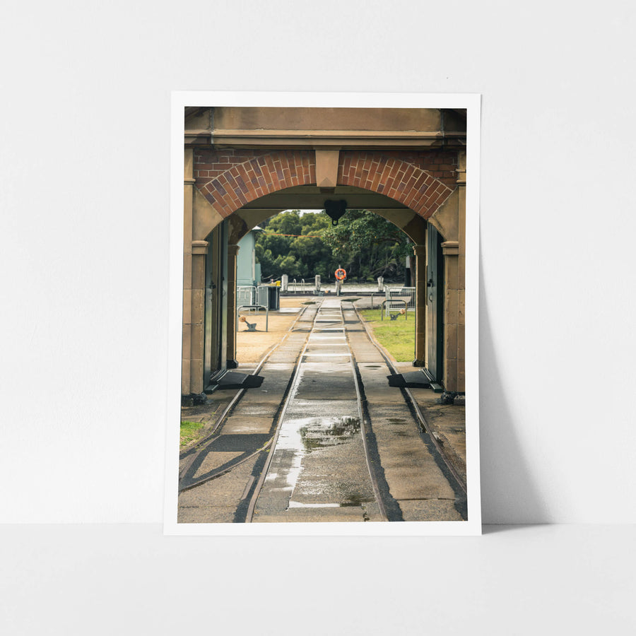 Entrance Rails at Newington Armory, narrow-gauge rail tracks run wet through a sandstone and brick archway, heading.
