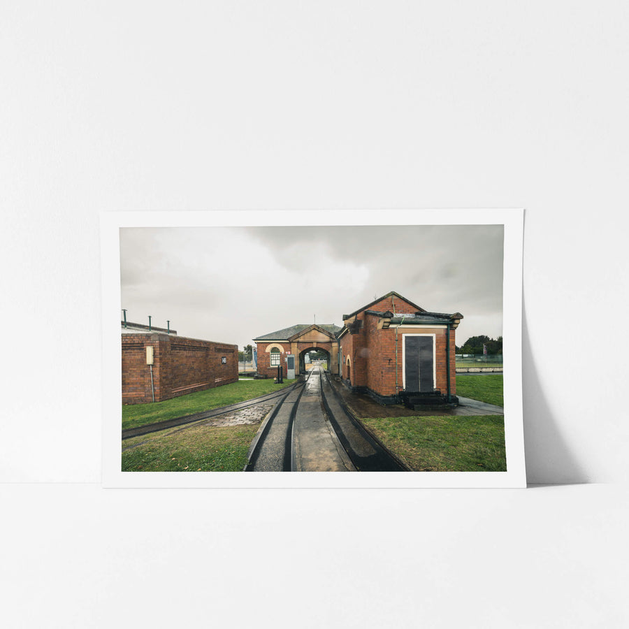 Entrance at Newington Armory, narrow-gauge rail lines run wet and black through a formal brick gatehouse at Newington Armory.