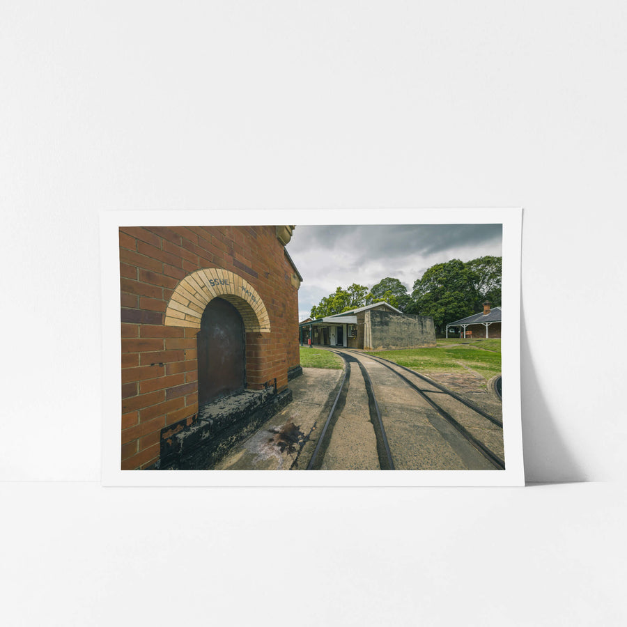 Rails at Newington Armory, narrow-gauge rails curve across a concrete apron, running past the issue hatch of a red brick.