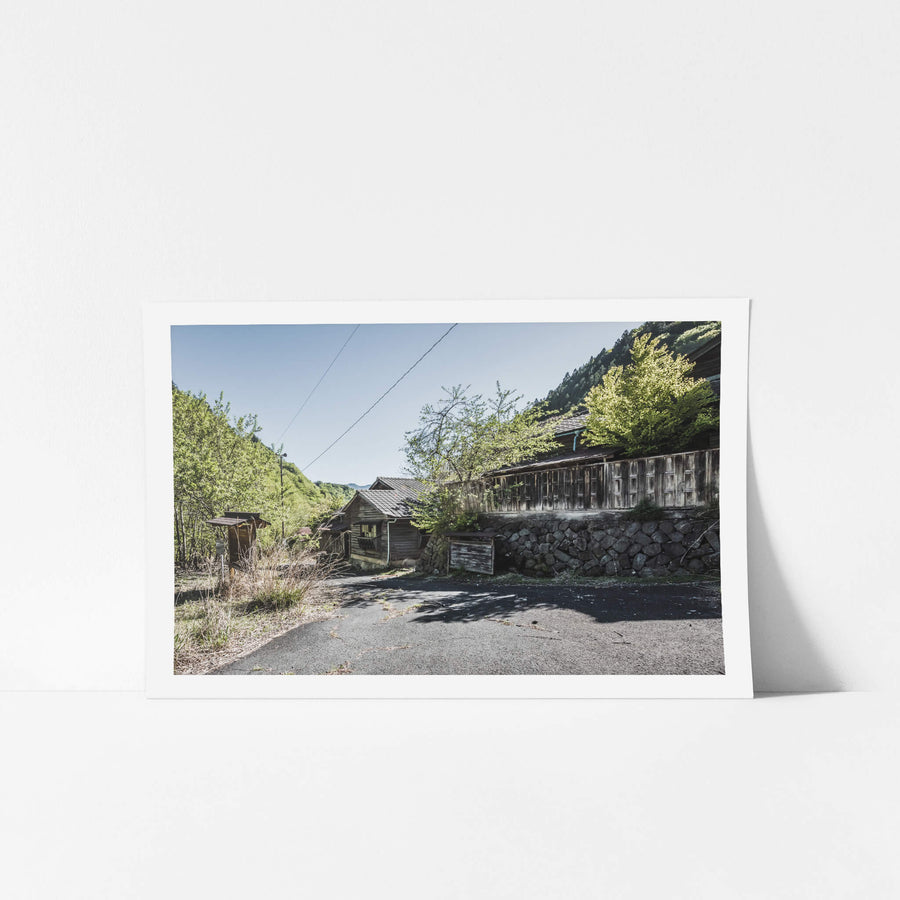 Main Entrance at Nichitsu Mining Village, weathered timber buildings line a narrow asphalt road that curves into the valley.
