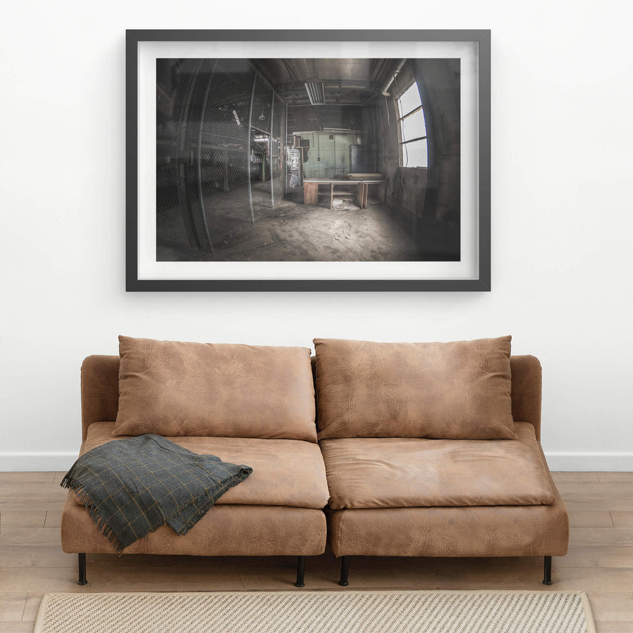 Caged Area at O-I Glass, a wooden desk sits near a large arched window, grey light falling across its surface.