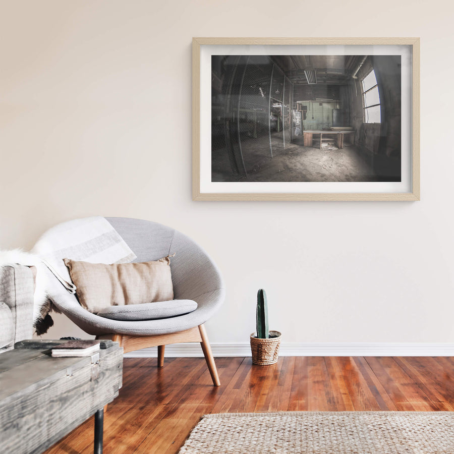 Caged Area at O-I Glass, a wooden desk sits near a large arched window, grey light falling across its surface.