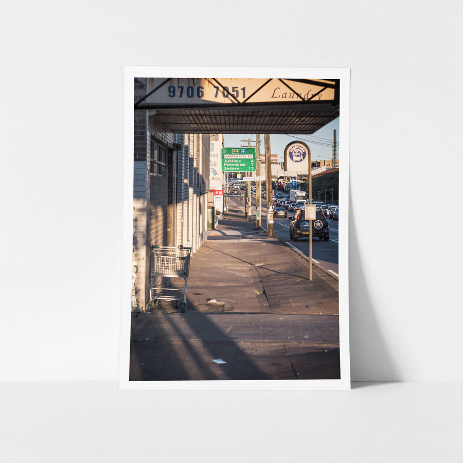 Heavy West Easy East at Parramatta Road, late afternoon light falls hard across the brick pavement under a laundry awning.